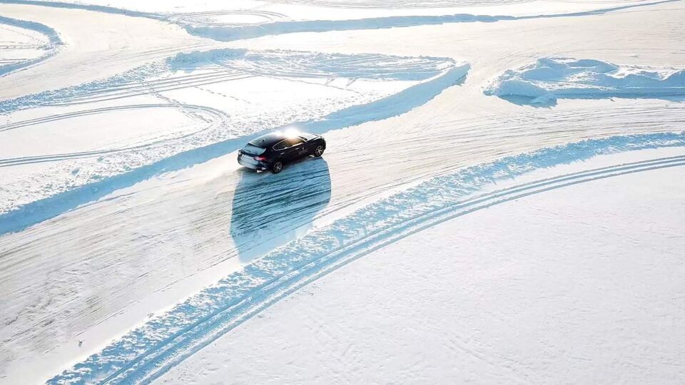Blue car drives by icy track on snow covered lake at winter. Aerial view. Sport car racing on snow race track in winter. Driving a race car on a snowy road.