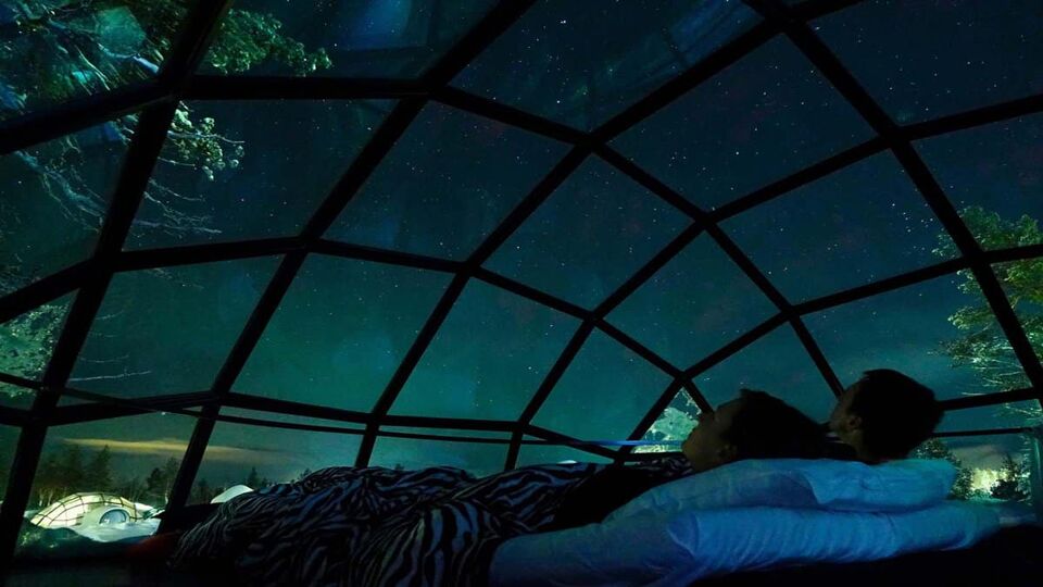 tourist couple observing the night sky from a cool glass house in the Scandinavian wilderness. Girlfriend and boyfriend enjoying a romantic evening in a cool glassy igloo.