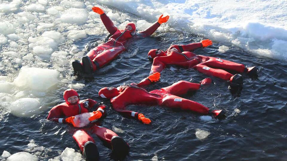 tourists in red thermal suits floating in the ice behind the sampo icebreaker
