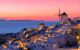 White Santorini buildings lit up at night with a pink and peach sunset in the background