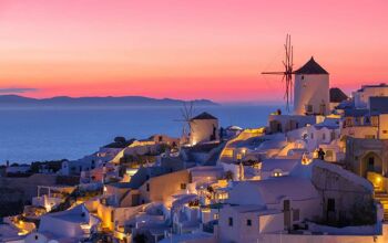 White Santorini buildings lit up at night with a pink and peach sunset in the background