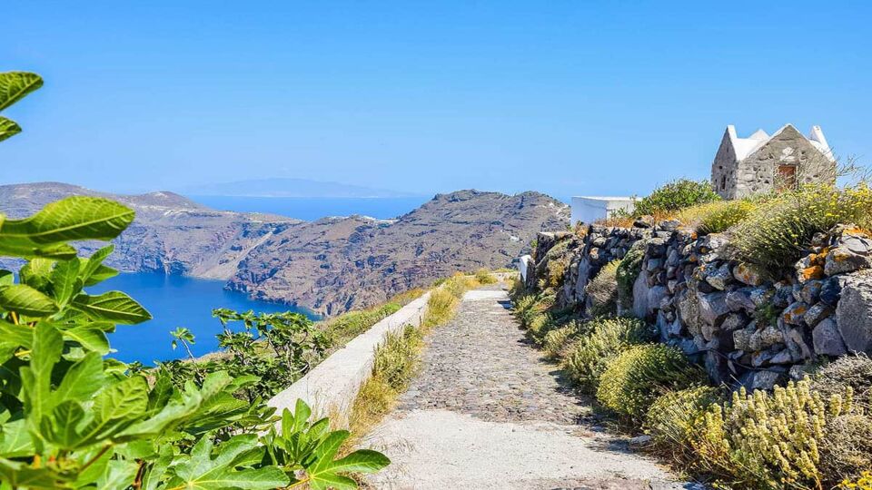 Landscape on the popular Fira to Oia hiking route, a path along the caldera with water visible to the left and greenery around
