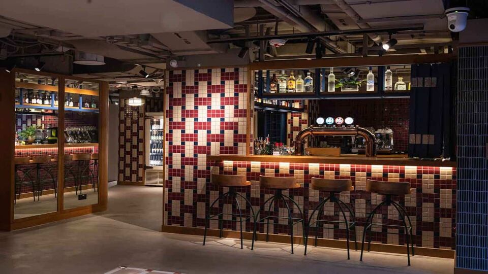 Dimly lit bar with red, cream and black tiling and tall bar stools