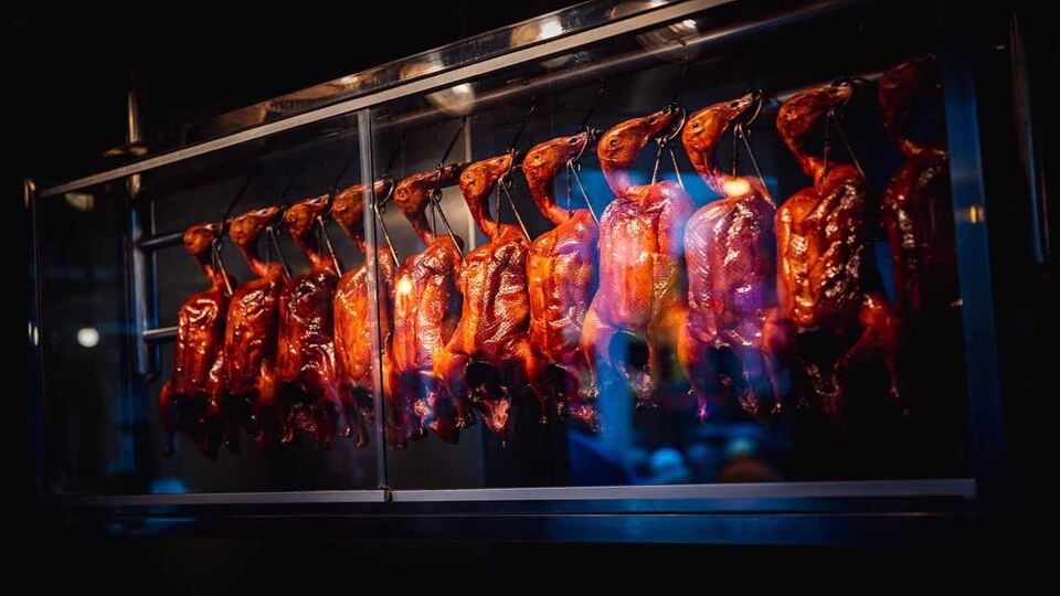 Row of Peking roasted ducks being sold, glowing in the light of street food stalls