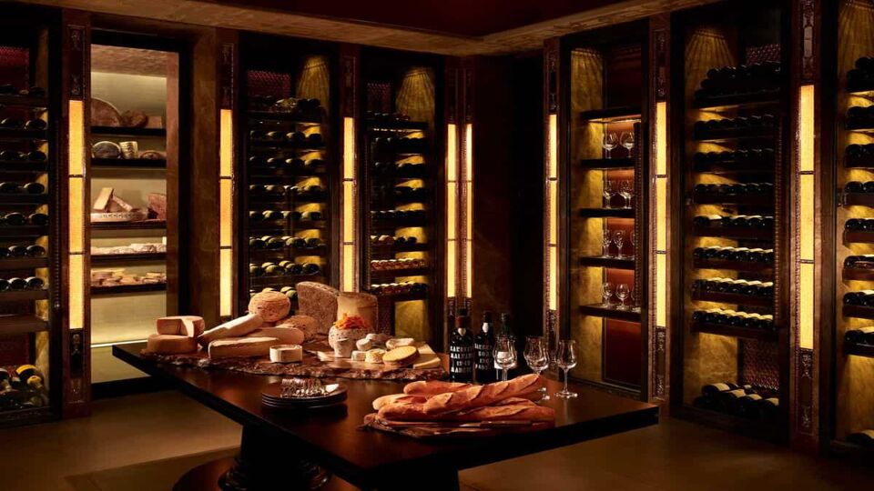 Bread, wine and cheeses set up on a table in a room surrounded by wine