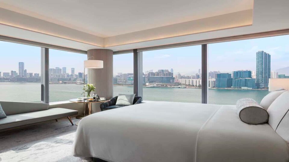 A large double bed, futon, and other furniture in a room with a 2 floor to ceiling windows with a view over the bay