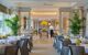 Bright dining area decorated with plants and yellow flowers, with a chef putting food on a table