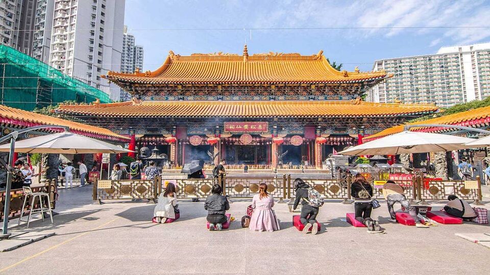 Exterior of the temple which has a golden roof and red and green paint. Smoking incense and praying people are visible