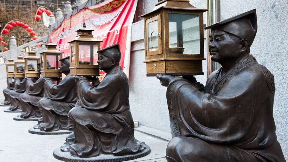 Row of Tao statues, each holding a glass lantern with a lit candle inside