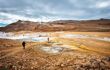 Hot fumaroles steam mud pots with people tourists at spring on trail path high wide angle view of geyser in geothermal area near lake Myvatn