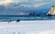 two riders on Icelandic horses crosses a snowy beach landscape