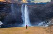 Seljalandsfoss waterfall in Iceland. Guy in red jacket looks at Seljalandsfoss waterfall.