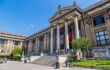 Exterior of large, neoclassical museum on a sunny day with steps eating up to four pillars and the entrance