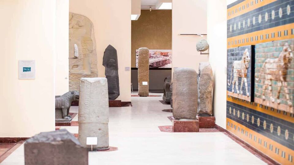 Interior of a museum with ancient, ruined columns dotting a hallway with one wall featuring a mosaic of a lion