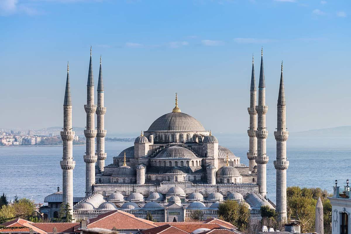 Aerial view of large mosque with six minarets with blue sea in the background