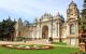 Ornate palace gate in front of formal flower beds and gravel pathways