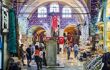 Interior of covered market with arched, tiled ceilings and Turkish flags hanging in the background as shoppers and shopkeepers wander through