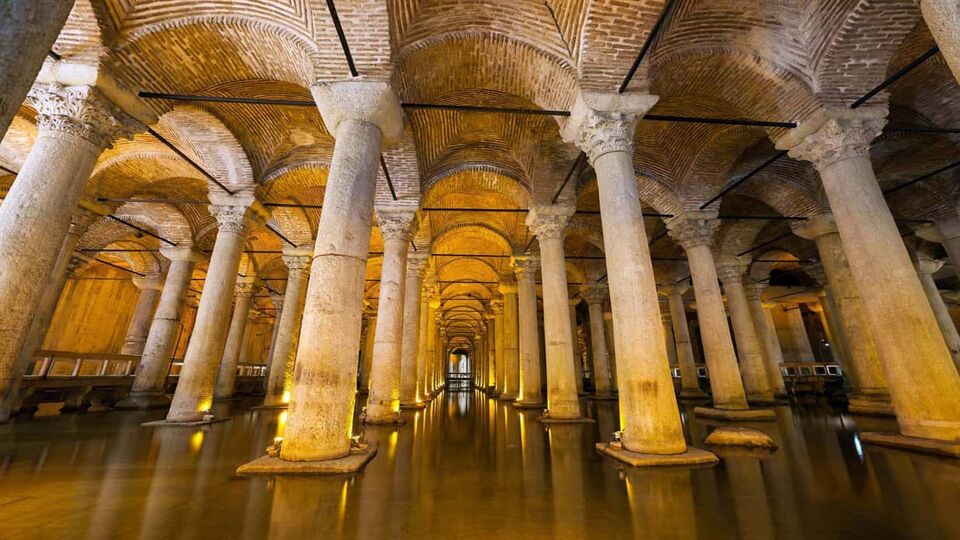 View of ancient cistern with arched ceilings. Columns rise from the ground to meet the ceiling and there is a thin layer of reflective water on the ground.