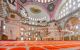 Interior of mosque with red-carpeted floors and low-hanging chandeliers