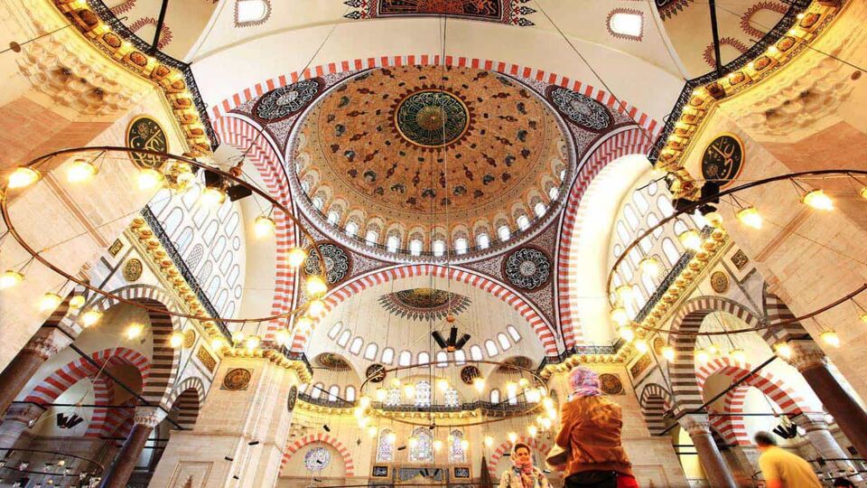 Interior of mosque with tiled domes and hanging chandeliers