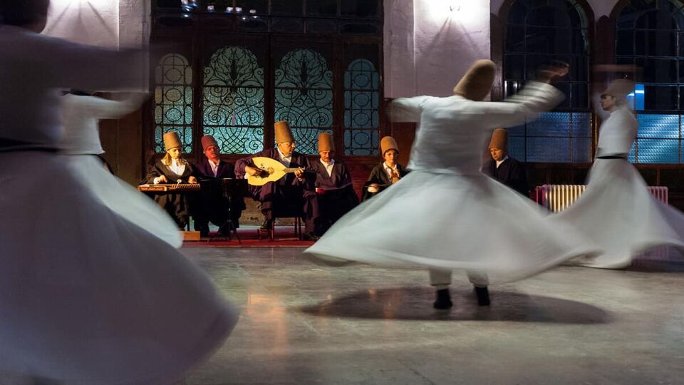 Turkish dancers in traditional, white skirts spin in front of musicians playing Turkish instruments and wearing conical hats