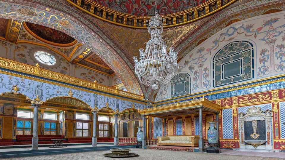 Ornate palace interior with tiled walls and chandelier hanging from the ceiling
