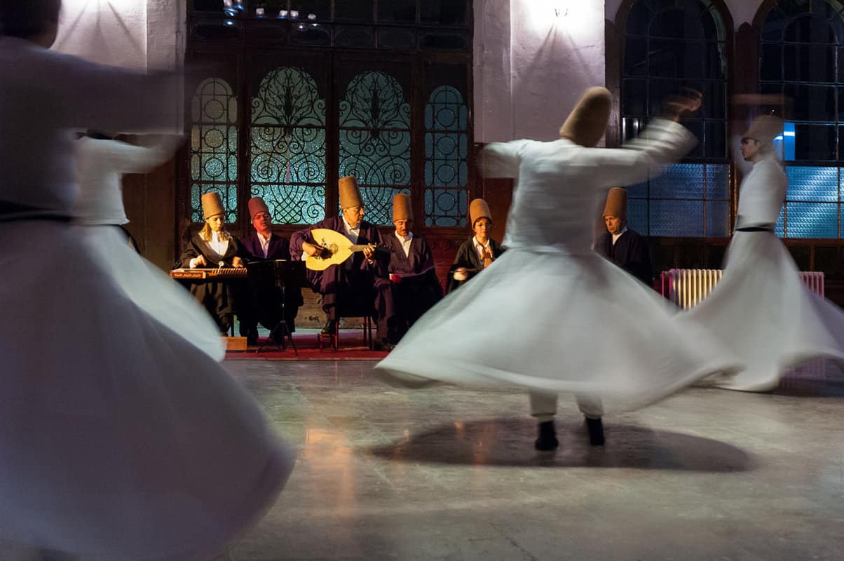 Dancers in white skirts whirling in front of traditional Turkish museums