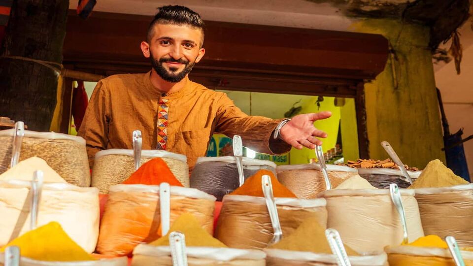 Market seller gesturing to piles of spices in store