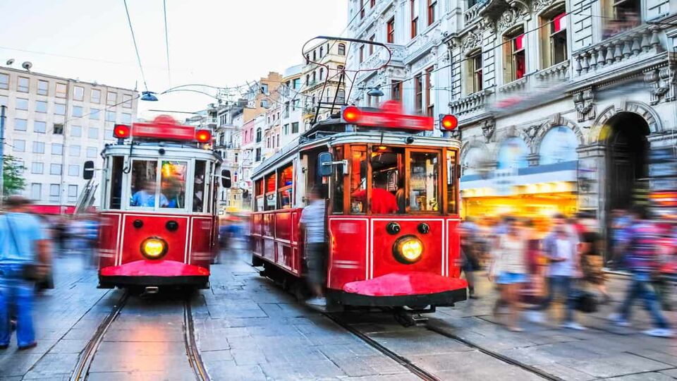 Two red trams moving down a crowded street