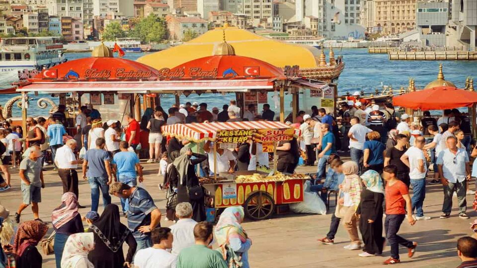 Crowded street with vendors selling food and the sea in the background