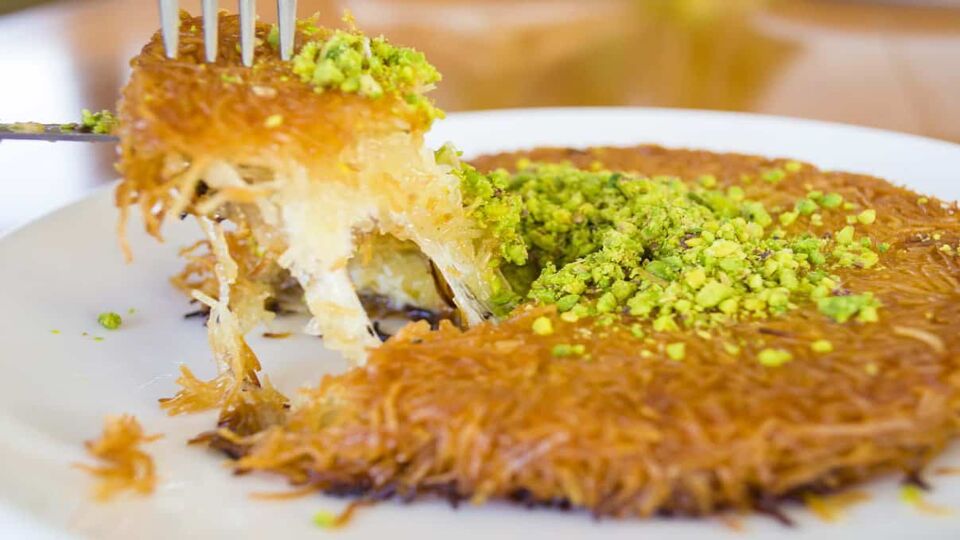 Turkish desert made of pistachio and cheese being lifted by a fork