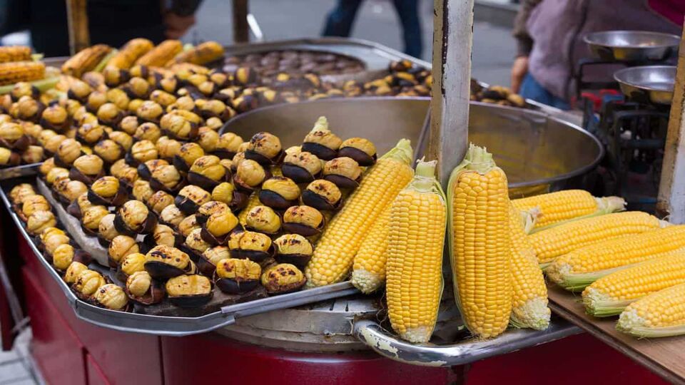 Street vendor's cart selling whole ears of corn and piles of roasted chestnuts