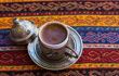Traditional Turkish Coffee in a ceramic coffee mug covered with copper pot on tablecloth with traditional texture and pattern