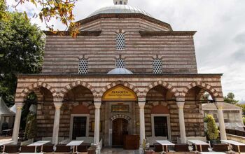 Exterior of a red and white brick Turkish bathhouse with cafe tables beneath the pillars at the front