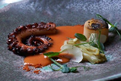 Close up of a plate with small octopus tentacle and orange sauce