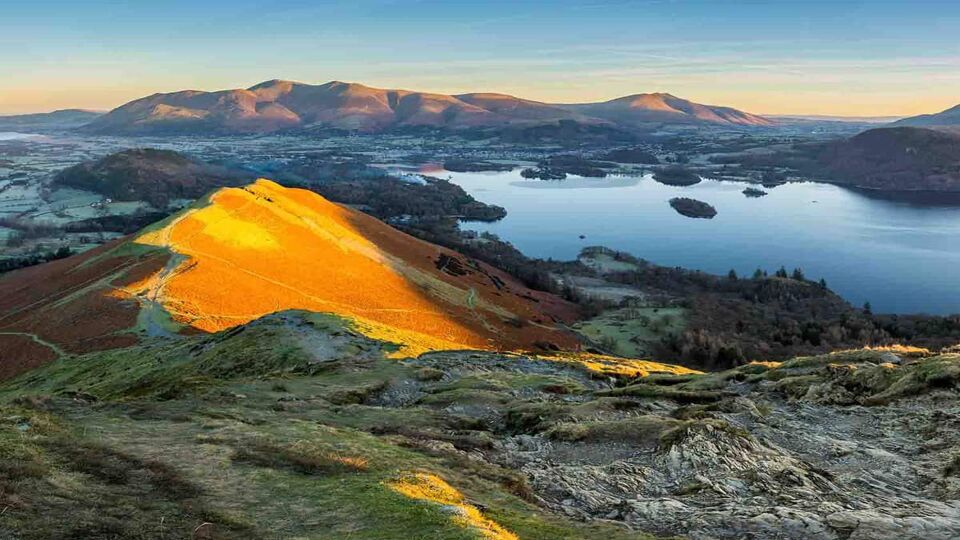 Panoramic view of Derwentwater in the Lake District with warm morning light illuminating Catbells.