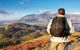 Man walking on Catbells mountain in the Lake District with a scenic panorama view of Derwentwater lake and Keswick in the background