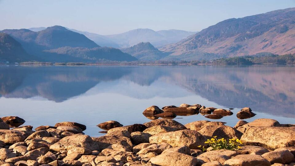 Soft morning light illuminates the Jaws of Borrowdale mountains, reflected in the calm waters of Derwent Water in the English Lake District.