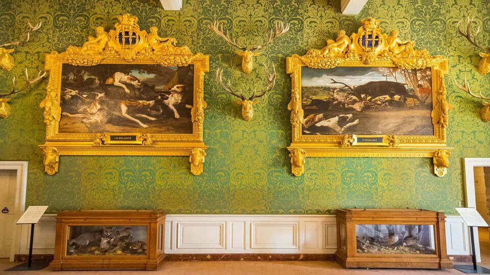 A green wall with two large, gold-framed paintings on the wall