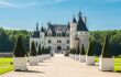 Exterior of the front of the chateau, with a tree-lined driveway in foreground