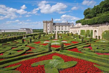 Red flowers and green shrubs in square hedged patterns in front of chateau