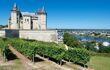 A side view of Saumur castle, with the vineyard in the foreground and Loire River in the distance