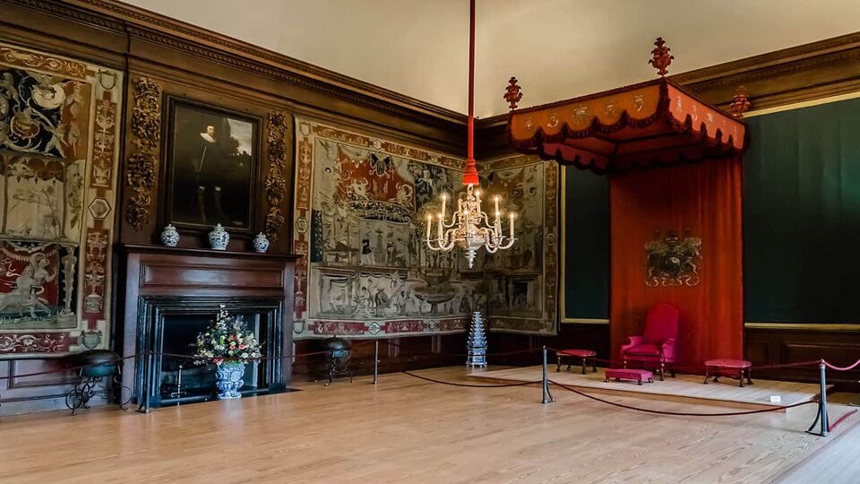 A room with a fireplace, a painting and a seat on the far right of the room