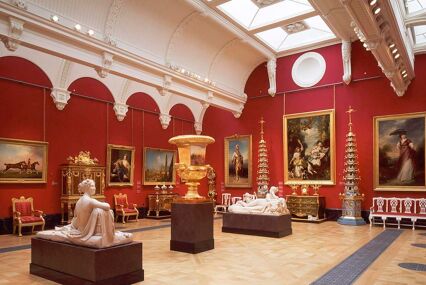 A bright red exhibition room with statues and furniture with gold accents