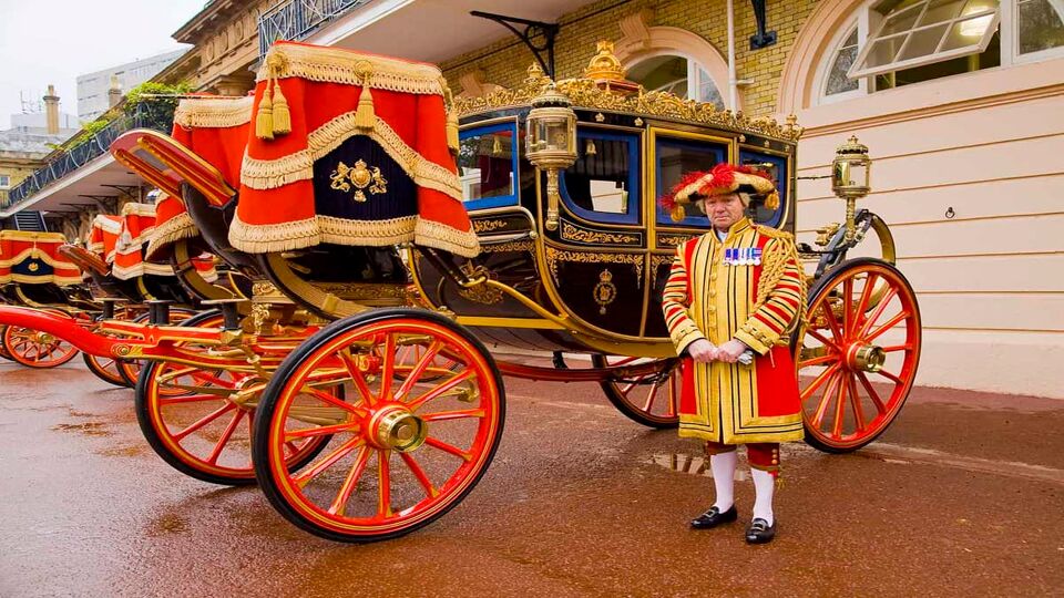A royal beefeater posing in front of a State Coach on a rainy day