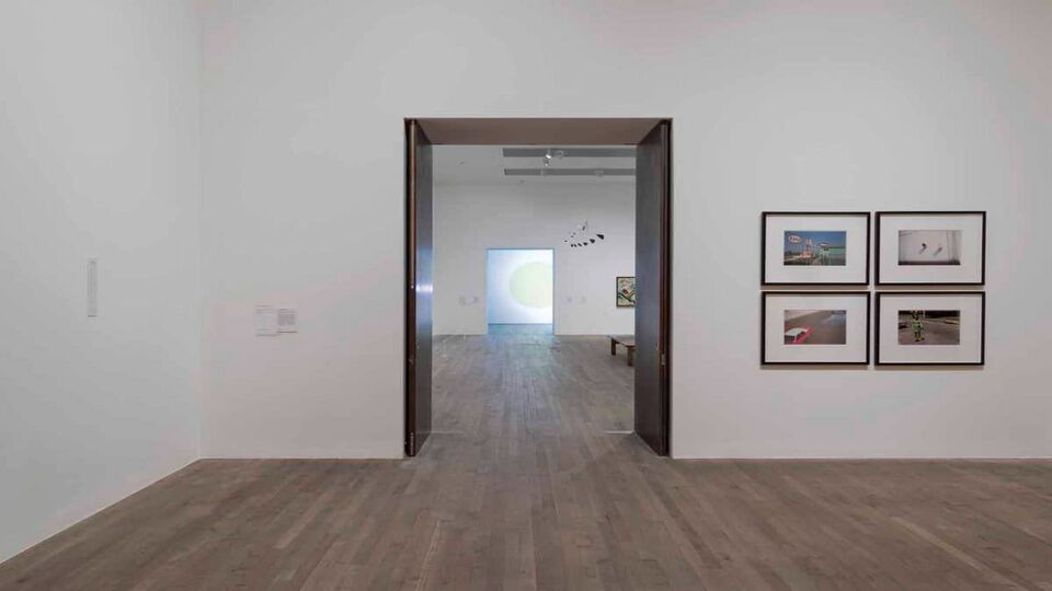 A white display room with four pictures on the wall leading to another display room