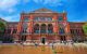 Rear exterior view of the beautiful red brick building on a sunny day. People paddling in the pool in foreground