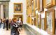 Side view close up of a woman staring at gold-framed paintings on the wall