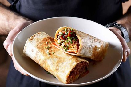 Close up of a man holding a plate with 2 delicious looking filled tacos