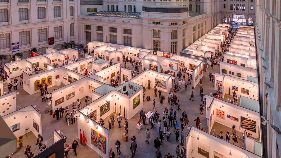 Aerial view down onto a large exhibition room filled with art stalls and lots of people wandering between them